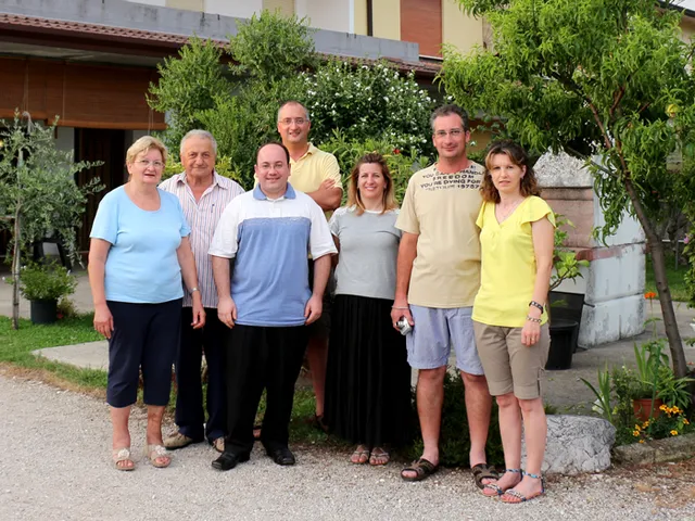 Sete parentes da Família Carlesso posando juntos em frente a uma casa na Itália.